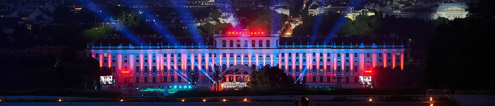 Schönbrunn Palace in Vienna lit up with colorful lights and spotlights during a nighttime event.
