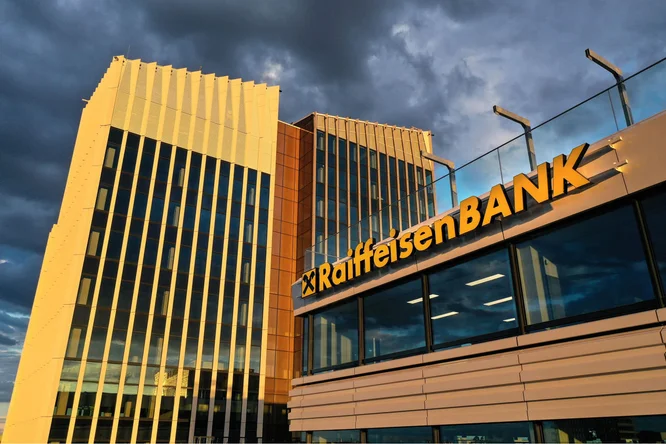 Das Bürogebäude der Raiffeisen Bank Ungarn besticht durch moderne Architektur mit reflektierendem Glas und beleuchteter Beschilderung. Das Gebäude ist in der Dämmerung unter einem dramatisch bewölkten Himmel aufgenommen.