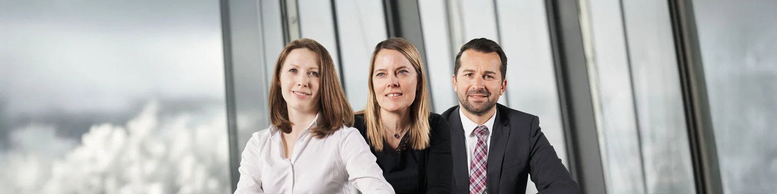 Three individuals dressed in business attire pose together, highlighting teamwork and professionalism in a corporate environment.