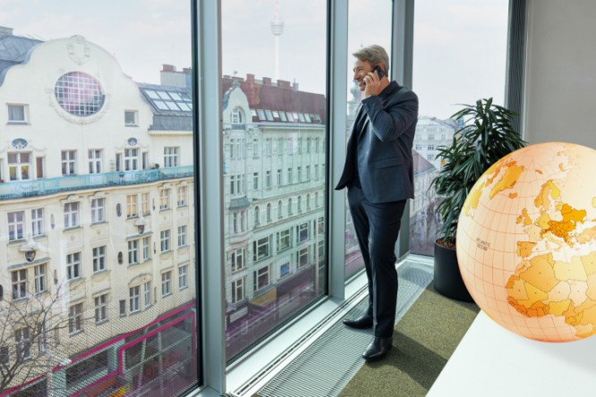 Man standing at the window looking outside with a large globe behind him