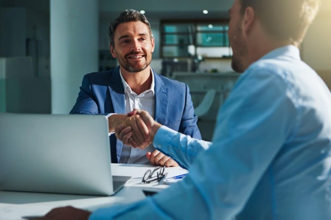 two men at a table shaking hands