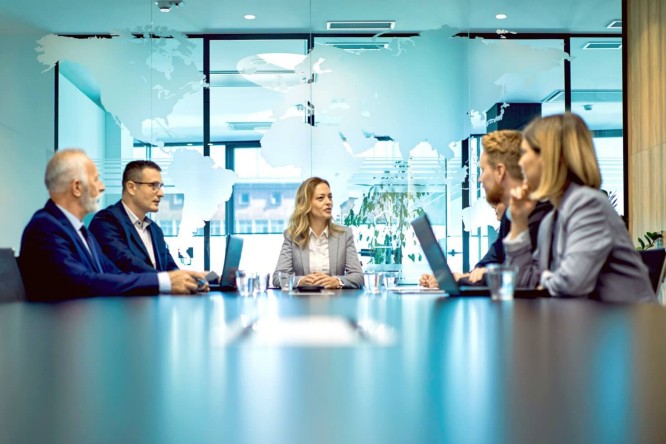 Geschäftsleute trafen sich zu einer Besprechung um einen Konferenztisch in einem modernen Büro, an dessen Glaswand eine Weltkarte prangte, die Teamarbeit, Strategie und globale Geschäftsaktivitäten verdeutlichte.