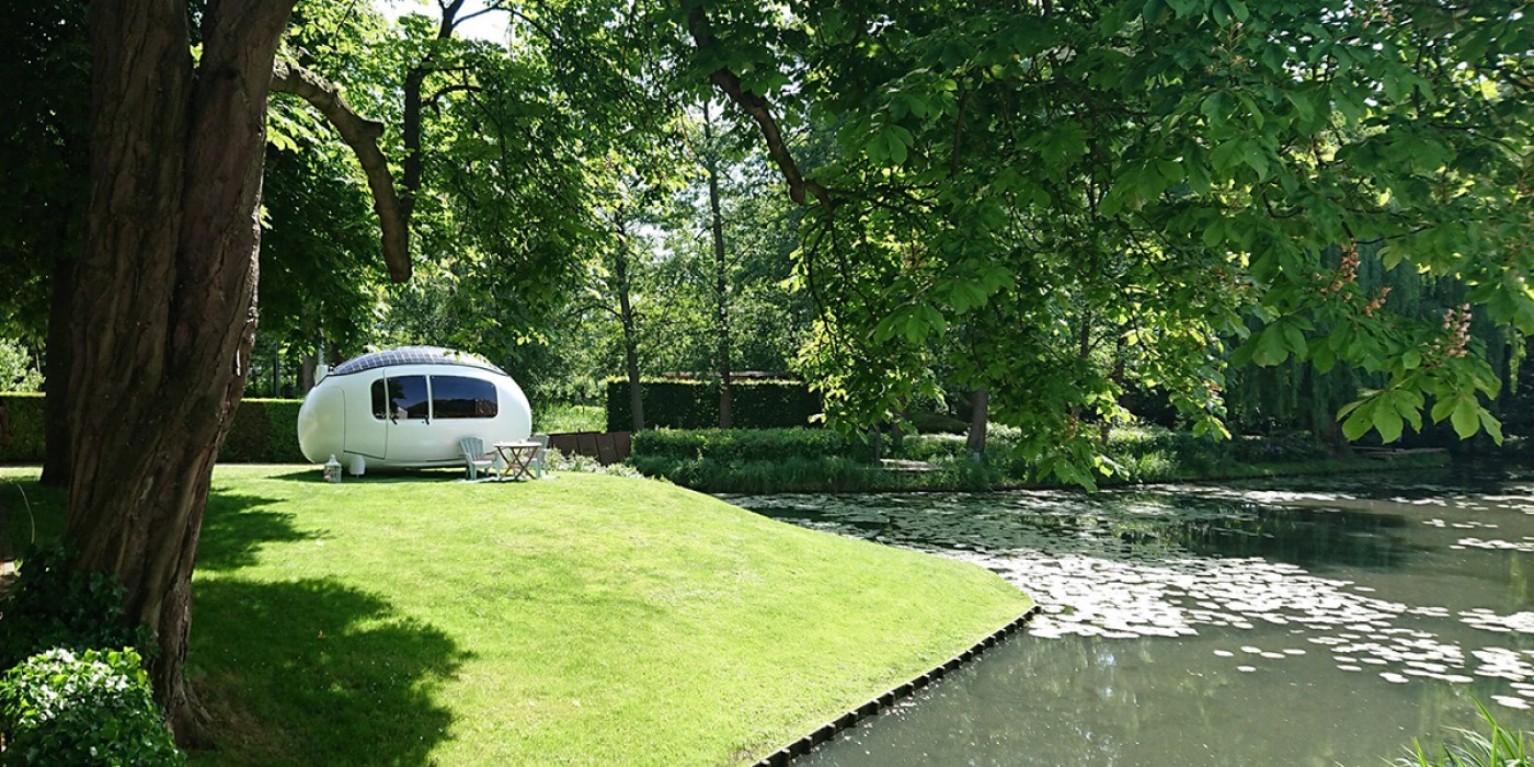 Ein elegantes, weißes, podförmiges Haus steht auf einem grünen Rasen neben einem ruhigen Teich, umgeben von üppigen Bäumen und Natur. (wird in einem neuen Tab geöffnet)