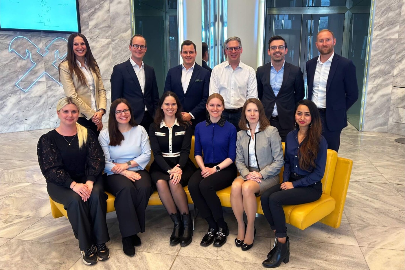 A group of Raiffeisen Bank employees in business attire posing for a team photo in a modern office setting.