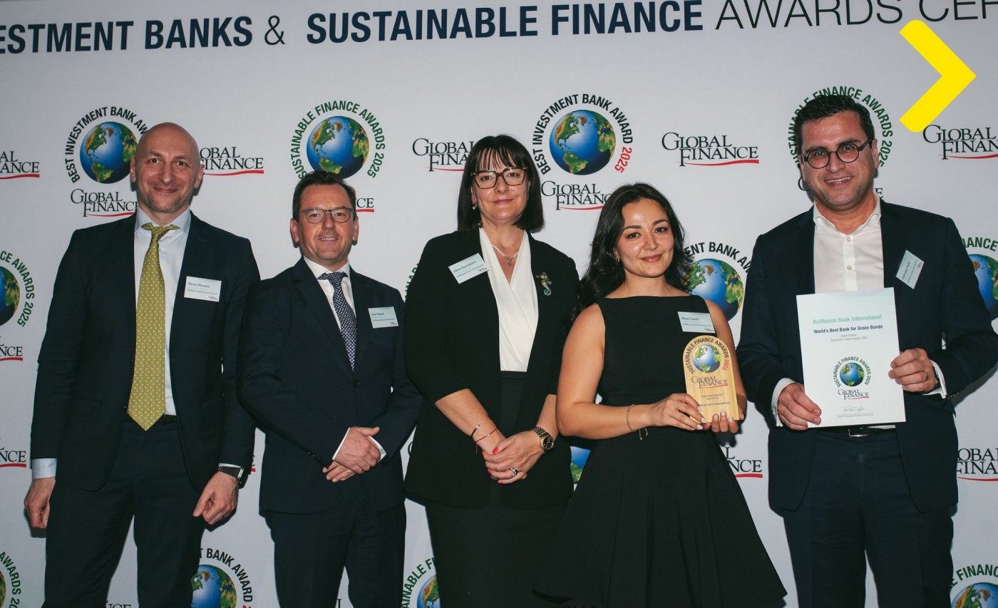 Eine Gruppe von Personen in formeller Kleidung steht bei einer Preisverleihung mit einer Trophäe und einer Urkunde vor einer Sustainable Finance Awards Fotowand.