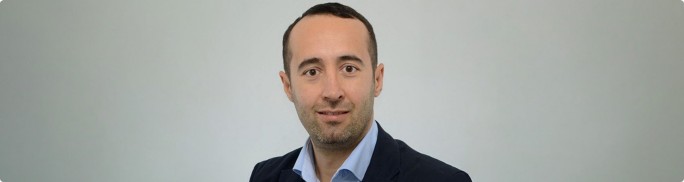 Portrait of Aliihsan Akgündüz in business attire with his face intentionally blurred for anonymity. Aliihsan is wearing a dark blazer over a light-colored shirt. The subject is posed against a plain, light gray background. The overall composition is simple and professional, suitable for corporate or privacy-related themes.