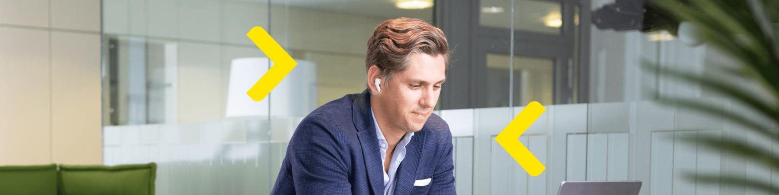 Ein Mann in einem blauen Blazer sitzt in einem modernen Büro an einem Schreibtisch und arbeitet an einem Laptop. Er trägt weiße Kopfhörer und scheint konzentriert auf seinen Bildschirm zu sein. Glaswände und moderne Möbel im Hintergrund deuten auf einen typischen Büroarbeitsplatz hin. Zwei leuchtend gelbe Pfeilgrafiken rahmen ihn ein und verleihen dem Ganzen eine dynamische Note.
