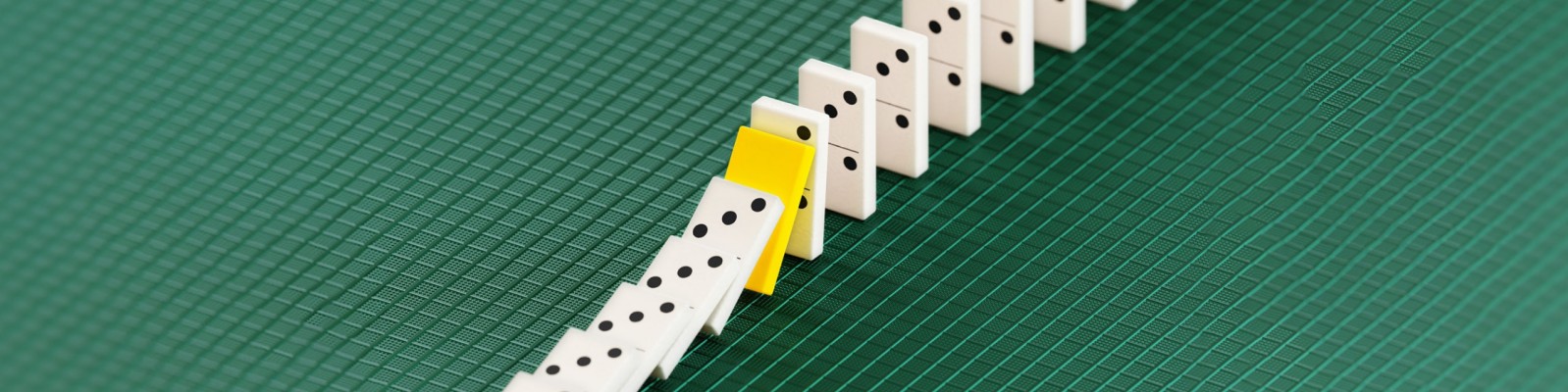 A row of white dominos with a single yellow domino on a green textured background, symbolizing the effect of optimized working capital