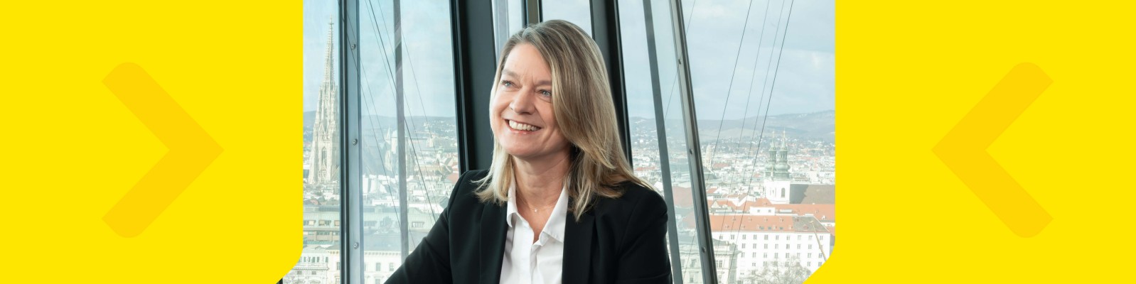 A woman in professional attire is seated in a contemporary office space with large glass windows. The background reveals a panoramic cityscape under daylight, suggesting a high-rise building setting. The image features a yellow graphic border with arrows on each side, adding a bold visual element. No visible text or numbers are present in the image.