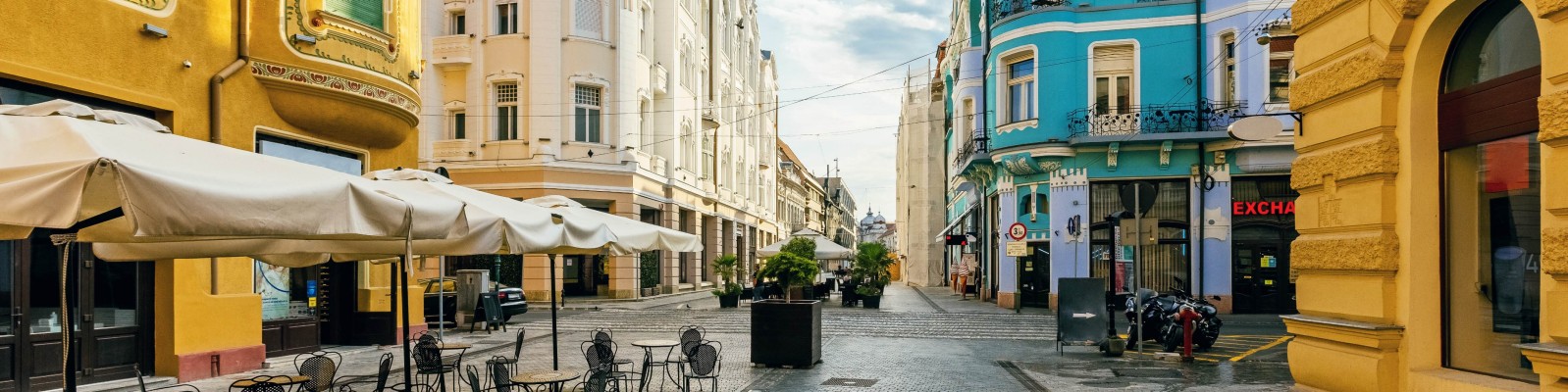 A picturesque street in Romania, featuring vibrant building facades in yellow and blue. The charming outdoor cafe seating and architectural details create a welcoming atmosphere for visitors.