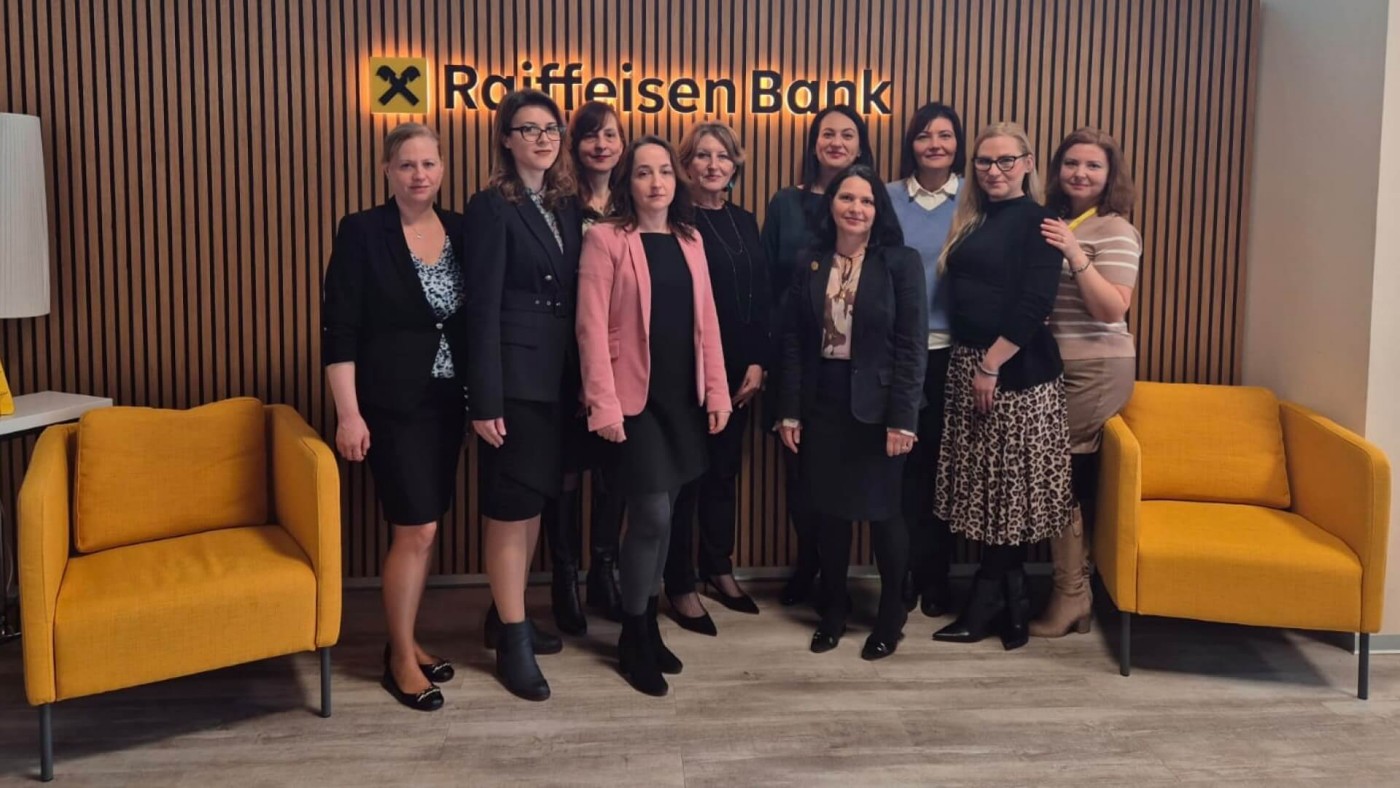 A group of professionals from Raiffeisen Bank gathered for a team photo in a modern office setting. The backdrop features the Raiffeisen Bank logo and stylish decor, highlighting a cohesive and professional team environment.