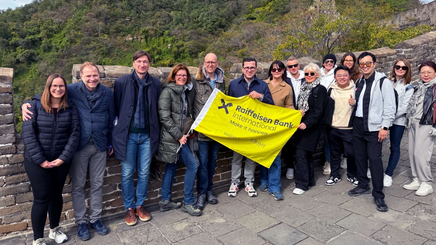 Eine Gruppe von Personen steht gemeinsam auf der Chinesischen Mauer und hält eine gelbe Raiffeisen Bank International Flagge.