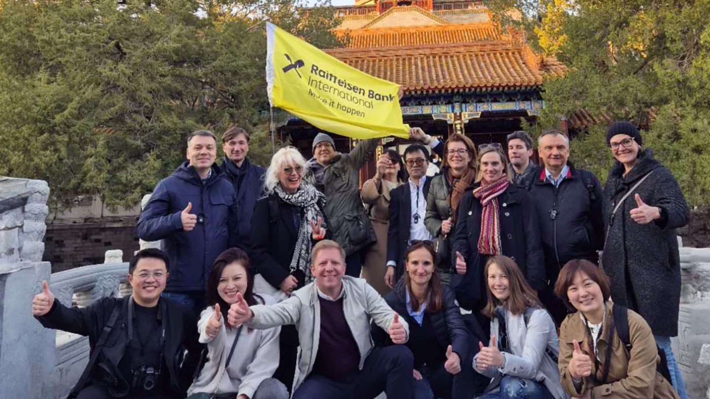 Eine vielfältige Gruppe von Menschen, die im Freien posieren, einige mit Daumen hoch, vor einem traditionellen chinesischen Gebäude und Bäumen im Hintergrund.