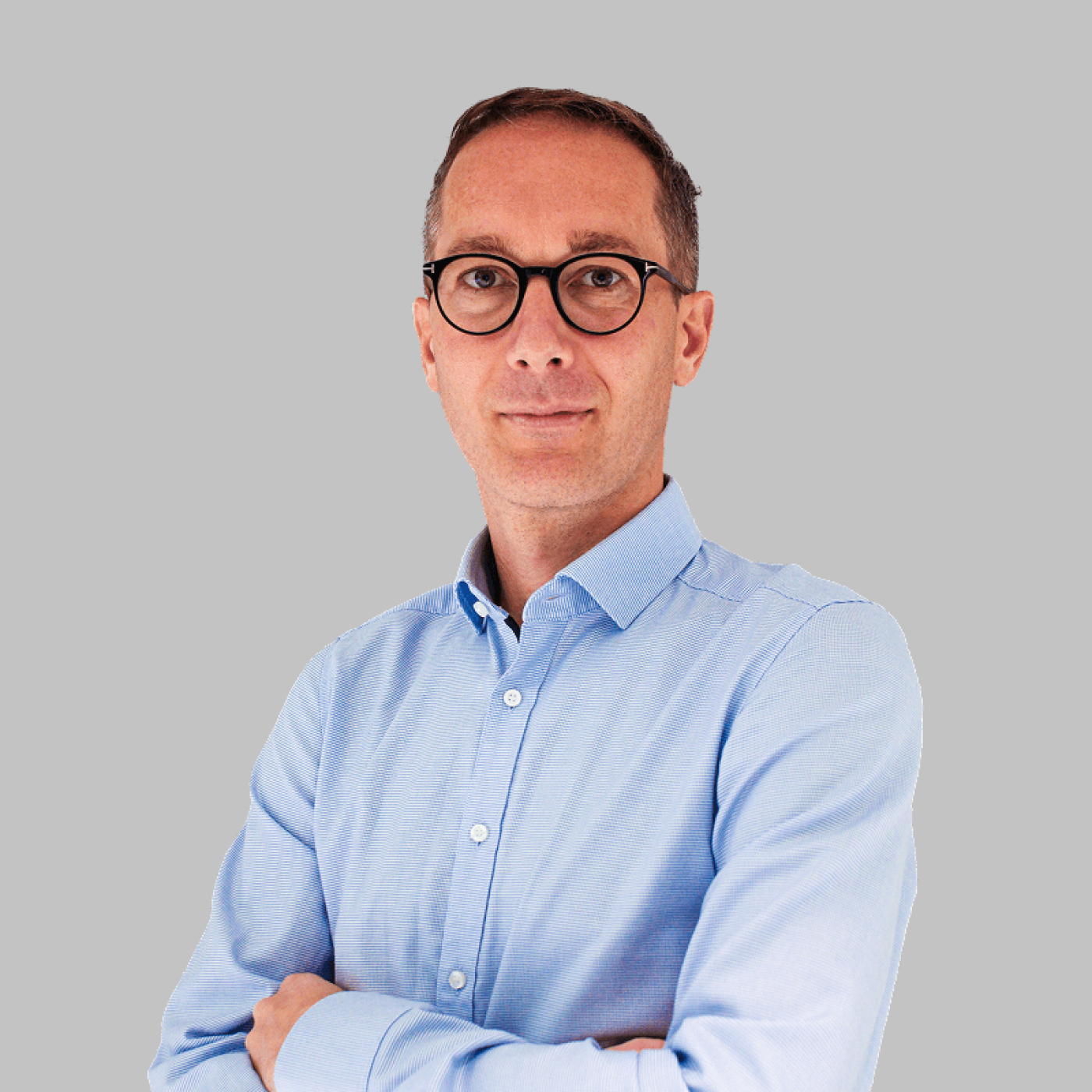 A person stands confidently with arms crossed, wearing a light blue shirt against a neutral grey background, exemplifying professionalism and self-assurance.