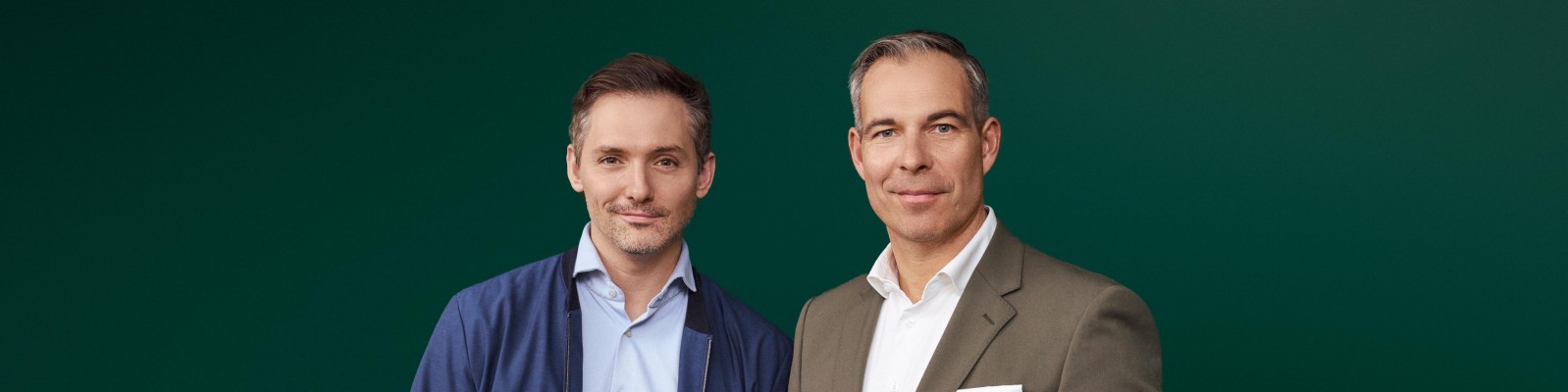 Henry Murray of waterdrop and Daniel Rath are dressed in formal attire, one wearing a blue blazer and shirt, and the other in a brown suit with a white shirt. The background is a solid green color, creating a professional and clean visual setting. The image emphasizes business or formal themes.