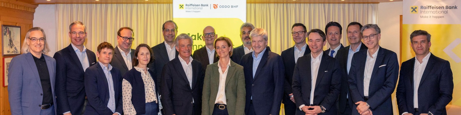 A group of professionals gathered at a Raiffeisen Bank International event, standing in front of branded banners and a curtain backdrop.