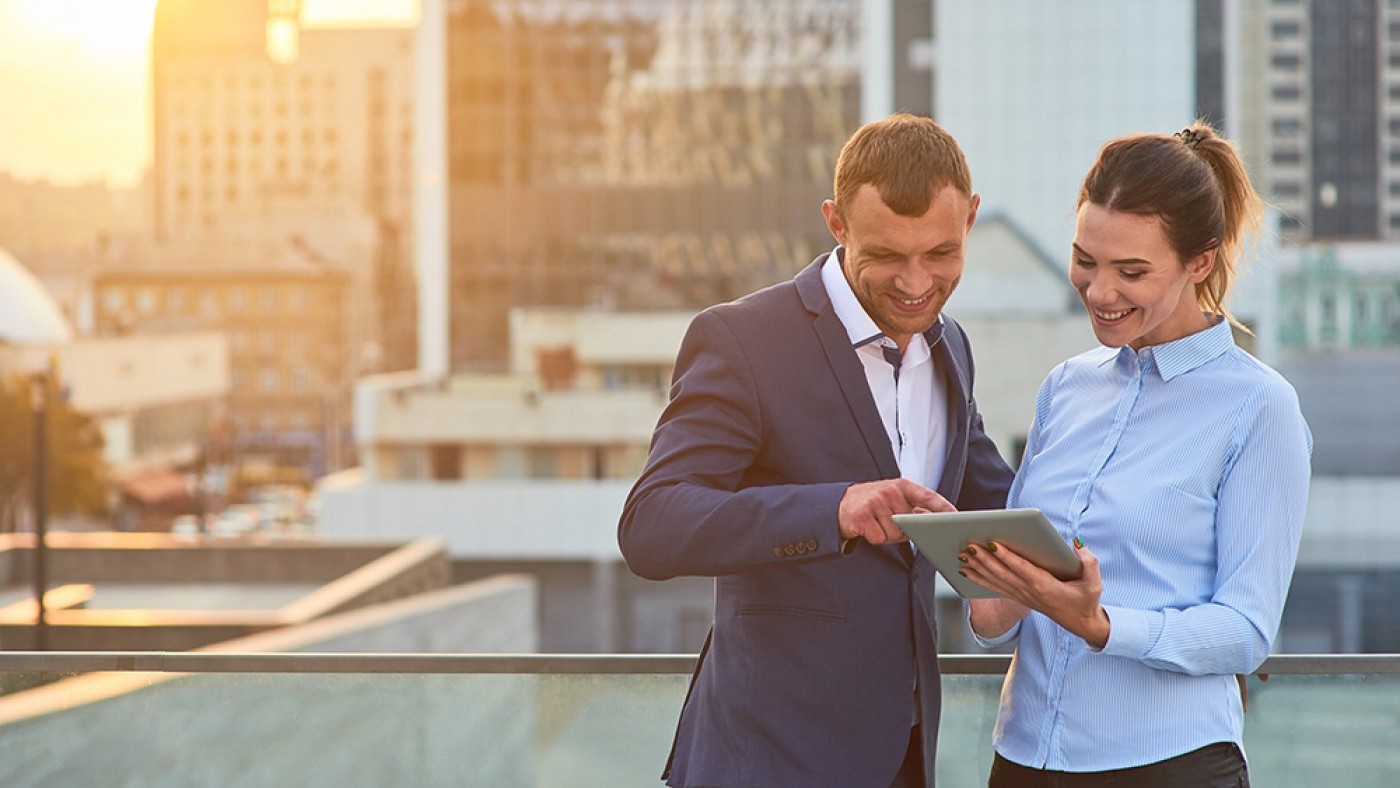 Man and woman smile into the iPad, office set-up in sunset