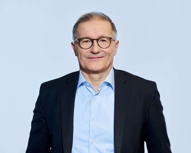 Porträt von Andreas Dorner, der ein dunkles Sakko und ein hellblaues Hemd trägt. Er steht mit einem leichten Lächeln in die Kamera und wirkt professionell und zugänglich. Der helle, einfarbige Hintergrund unterstreicht die geschäftliche Atmosphäre. Das Bild ist gut ausgeleuchtet und neutral gestaltet und eignet sich daher für professionelle Porträts von Führungskräften.