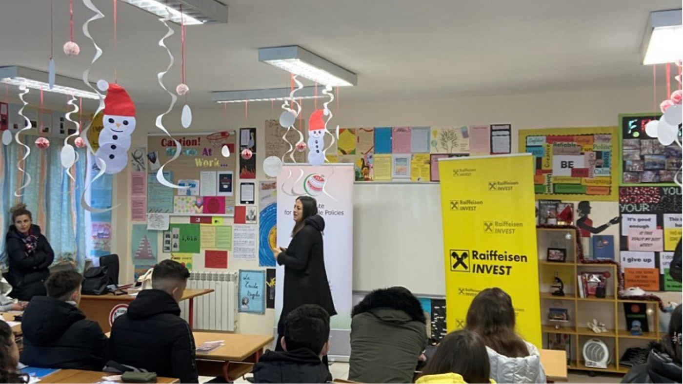 Ein Klassenzimmer, festlich mit Schneemännern dekoriert, in dem eine Präsentation stattfindet. Zu sehen sind Banner von Raiffeisen Invest und dem Institut für nachhaltige Politik.