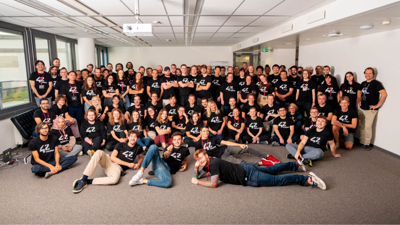 Eine große Gruppe von Menschen versammelt sich für ein Teamfoto – alle tragen schwarze T-Shirts mit der Aufschrift „42 Vienna“.