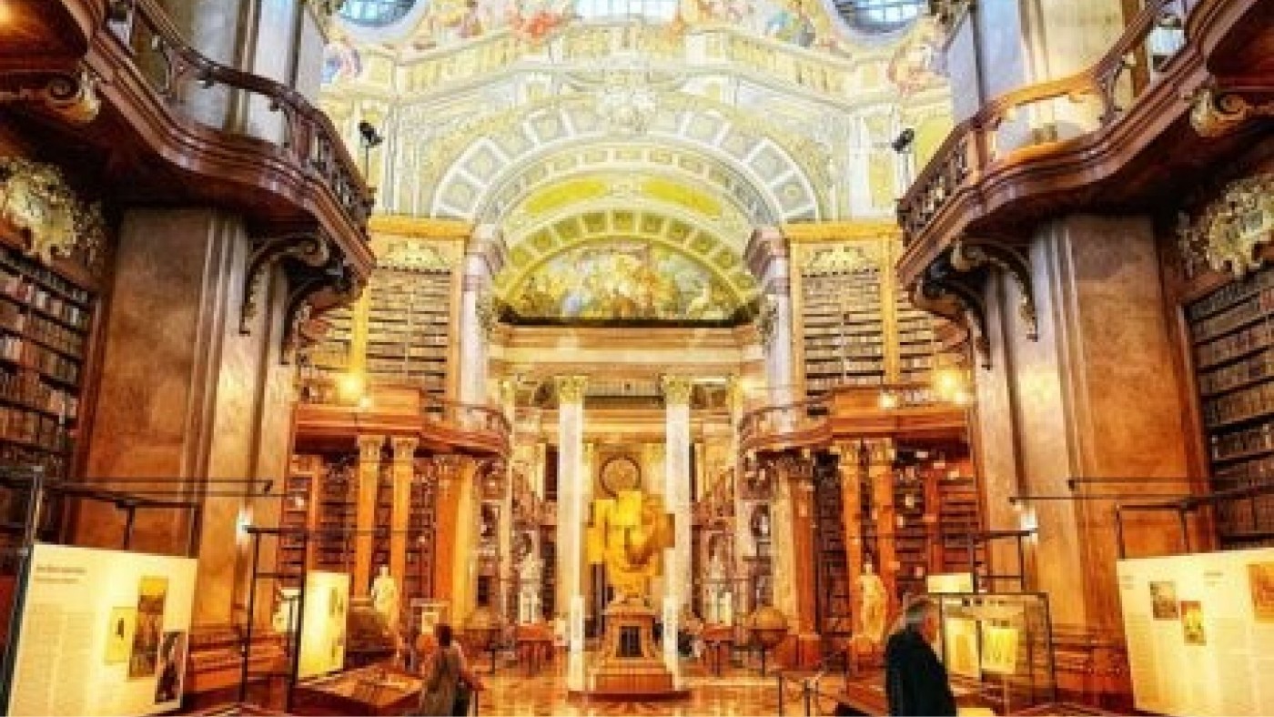 Beeindruckender Blick ins Innere einer großen Bibliothek mit prachtvoller Architektur, Bücherregalen und künstlerisch gestaltetem Deckenschmuck.