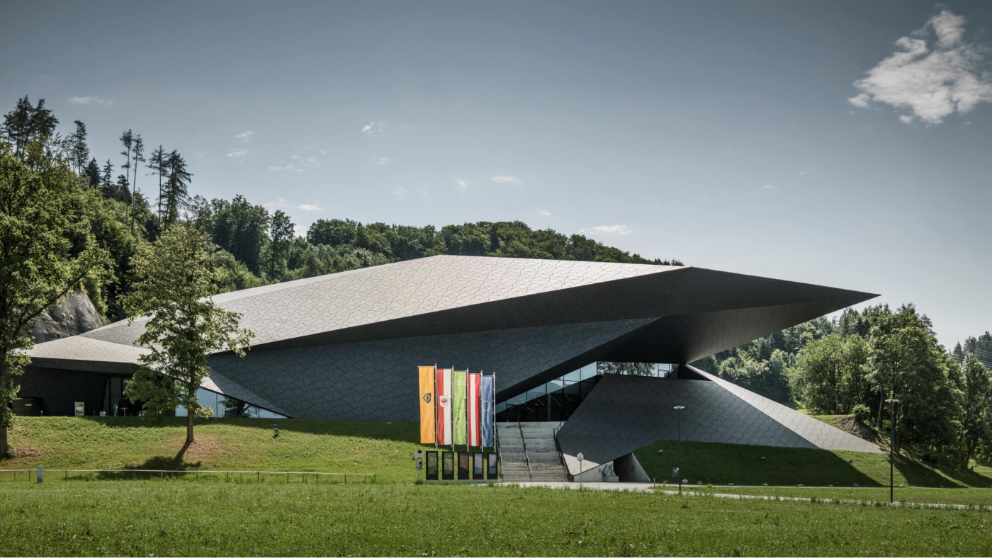 Auffälliges, modernes Gebäude mit kantigen Designelementen, umgeben von üppigem Grün und Bäumen.