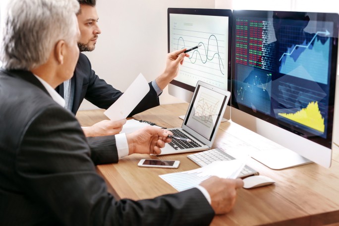 Fachleute analysieren Finanz- und Marktdaten auf mehreren Bildschirmen und besprechen Trends sowie Leistungskennzahlen in einer modernen Büroumgebung.