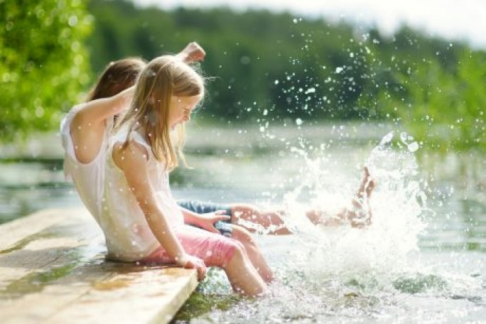 Zwei Kinder planschen mit den Füßen an einem See.