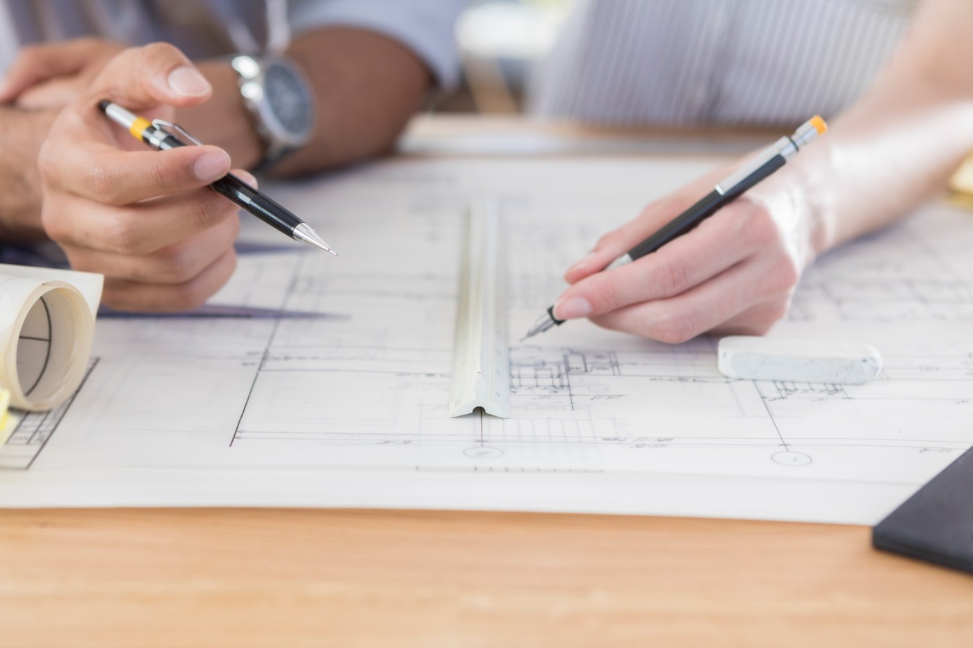 Unrecognizable male and female architects use ruler as they draw on a blueprint. They are both holding mechanical pencils.