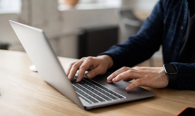 Nahaufnahme von Händen, die an einem Holzschreibtisch in einer modernen Büroumgebung auf einem Laptop tippen, um Produktivität, Remote-Arbeit und digitale Kommunikation zu veranschaulichen.